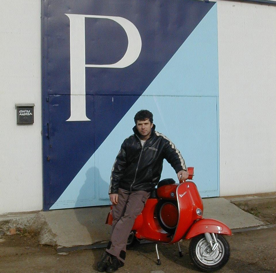 Andrea davanti alla sua officina con una Vespa rossa